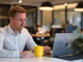 Mężczyzna z kubkiem kawy zastanawia się, dlaczego internet wolno chodzi, patrząc na ekran laptopa w biurze.