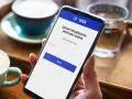 Kobieta używa telefonu do łatwej i bezpiecznej płatności kartą w internecie. Na ekranie widnieje logo VISA i pole do wpisania adresu e-mail.