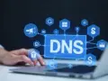 Grafika przedstawia sieć połączonych ikon wokół napisu DNS, symbolizując propagację DNS i zarządzanie domenami.