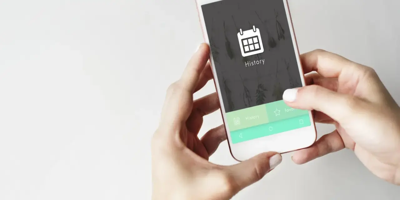 Dłonie trzymają telefon, na ekranie którego widnieje ikona kalendarza i napis "History". Czas na usuń historię przeglądania w telefonie.