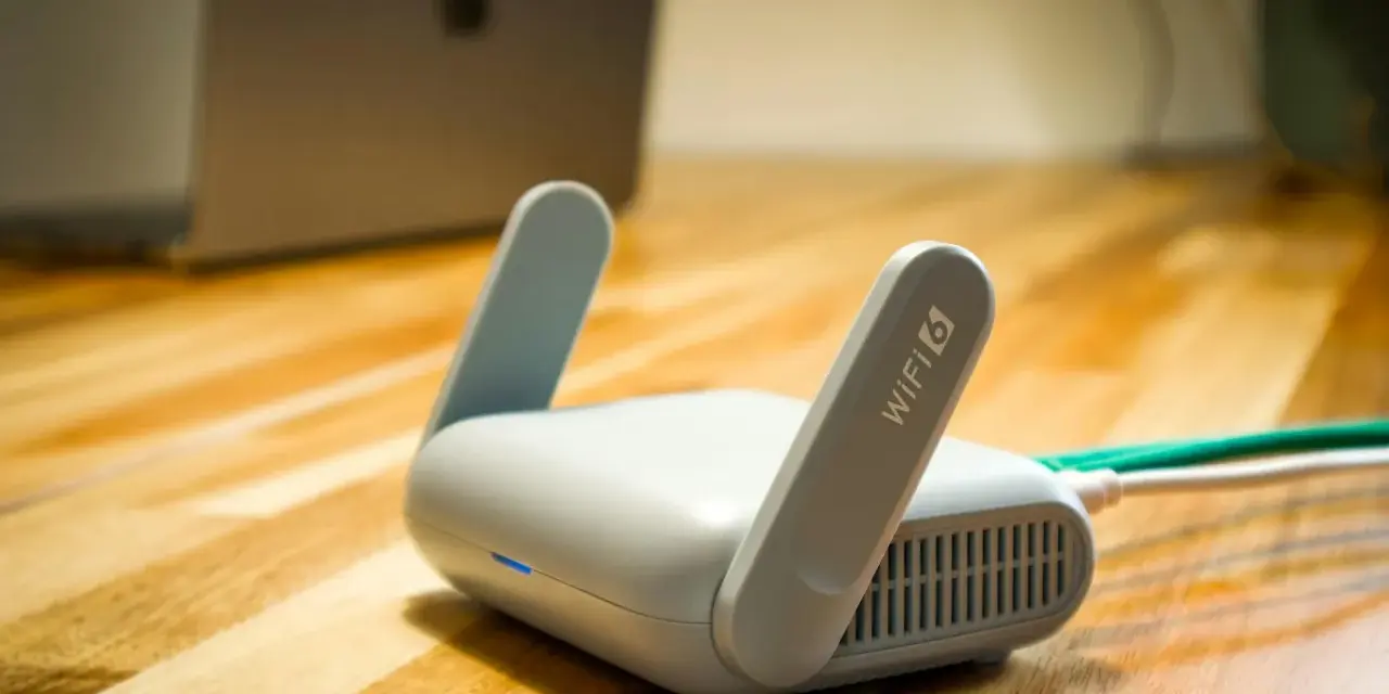 Router Wi-Fi 6 z antenkami, obok laptopa. Czy wiesz, upnp co to? Ułatwia komunikację urządzeń w sieci.