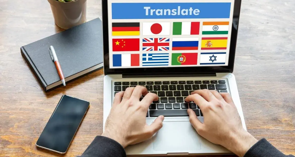 Ręce piszą na laptopie z widoczną wtyczką do tłumaczenia stron i flagami wielu krajów.