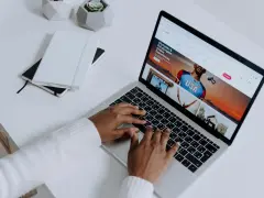 Osoba pisze na klawiaturze laptopa, na ekranie którego widać stronę z ofertami podróży. Przeglądarki internetowe otwierają świat możliwości.
