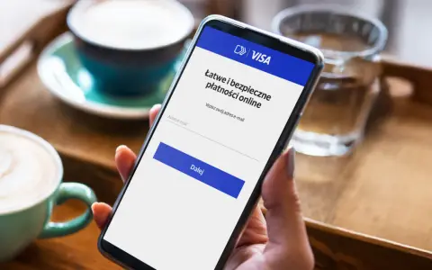 Kobieta używa telefonu do łatwej i bezpiecznej płatności kartą w internecie. Na ekranie widnieje logo VISA i pole do wpisania adresu e-mail.