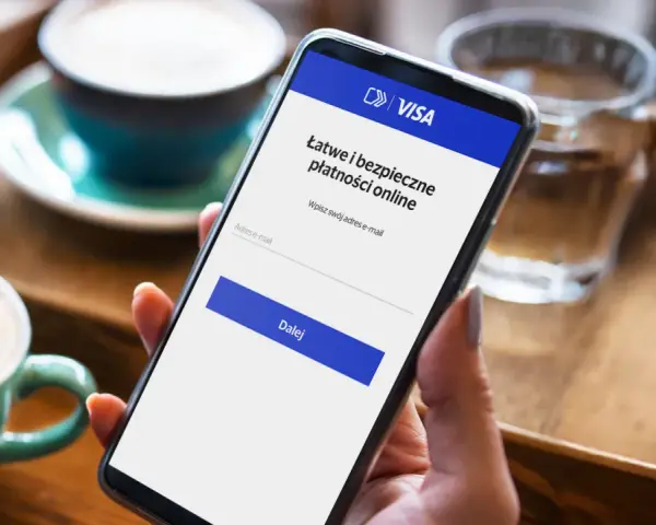Kobieta używa telefonu do łatwej i bezpiecznej płatności kartą w internecie. Na ekranie widnieje logo VISA i pole do wpisania adresu e-mail.