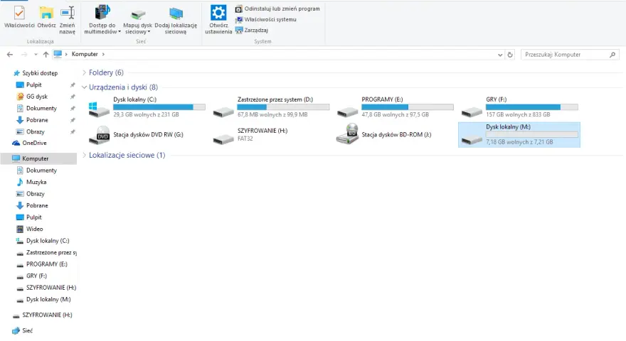 Widok folderów systemu Windows, gdzie widać dyski, w tym "SZYFROWANIE (H:)", co może być pomocne, gdy zastanawiasz się, jak zaszyfrować folder.