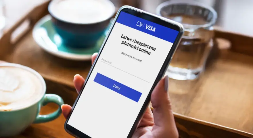 Kobieta używa telefonu do łatwej i bezpiecznej płatności kartą w internecie. Na ekranie widnieje logo VISA i pole do wpisania adresu e-mail.