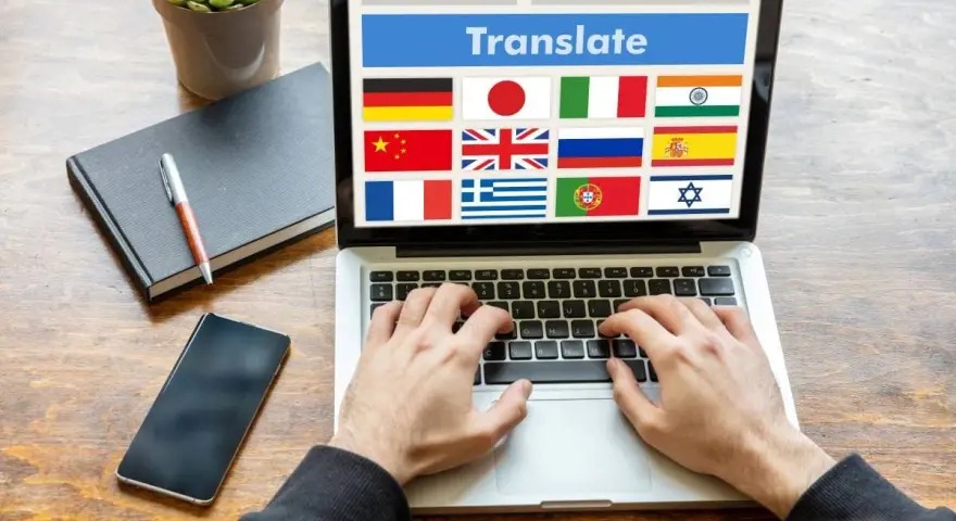 Ręce piszą na laptopie z widoczną wtyczką do tłumaczenia stron i flagami wielu krajów.