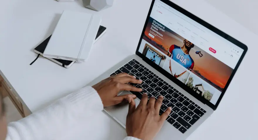 Osoba pisze na klawiaturze laptopa, na ekranie którego widać stronę z ofertami podróży. Przeglądarki internetowe otwierają świat możliwości.