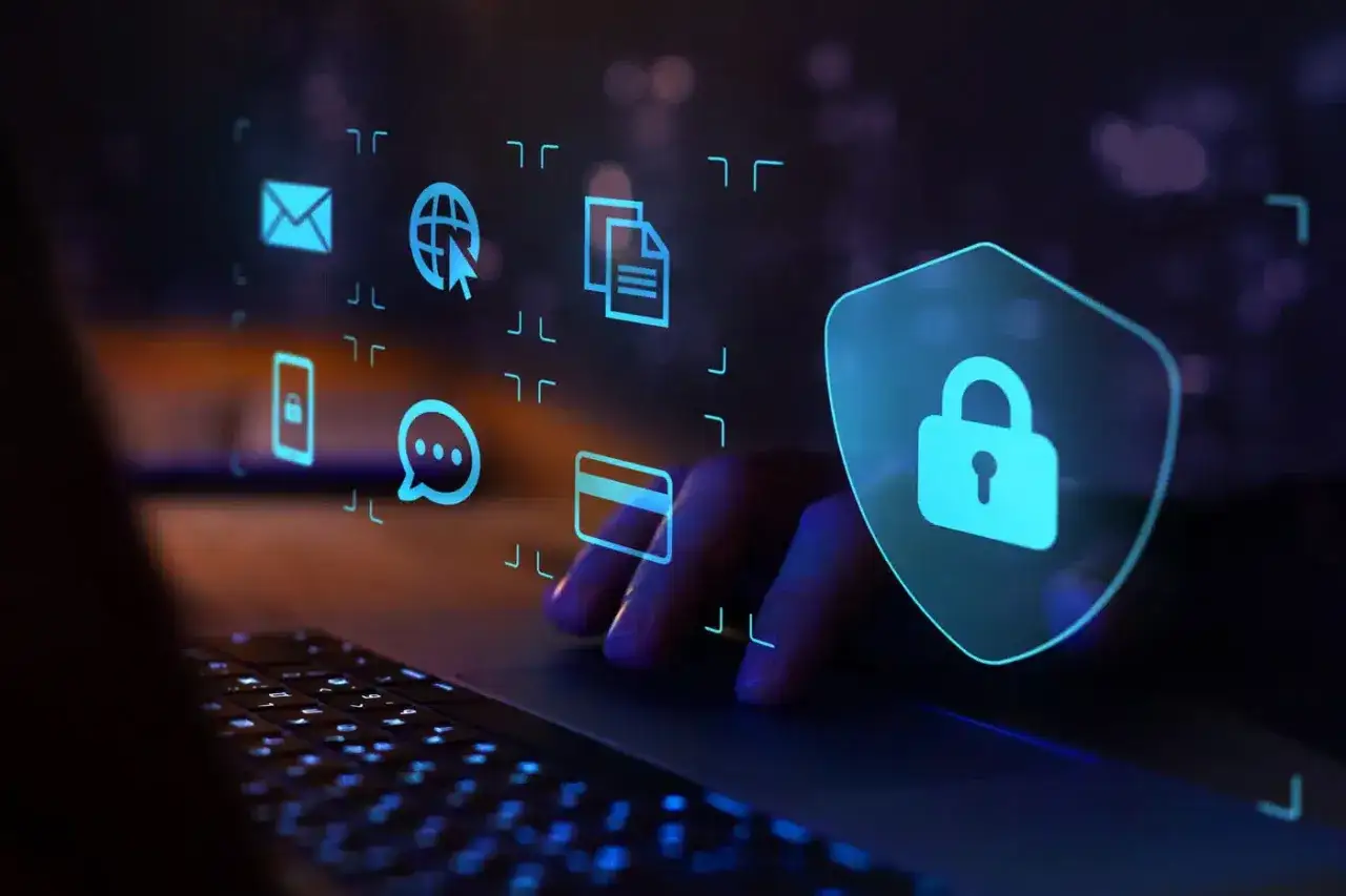 Ręce na klawiaturze, nad nimi cyfrowe ikony: poczta, globus, dokumenty, telefon, czat, karta płatnicza. Tarcza z kłódką symbolizuje ochronę przed wirusem internetowym.